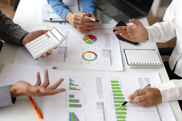 Business team collaborating and analyzing financial charts while using calculators and taking notes during an office meeting at the desk, strategy and planning.