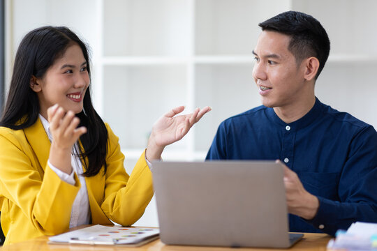 Asian businesswoman gesturing with hands while talking and smiling to businessman in meeting room during business meeting.