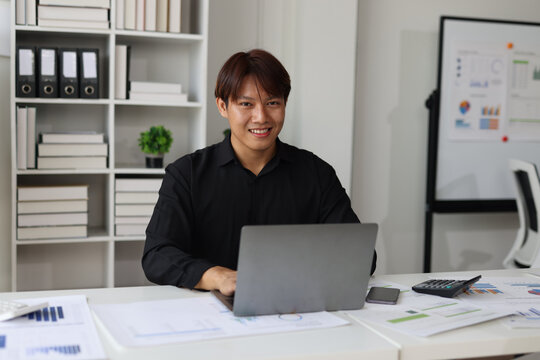 Asian businessman working with laptop and analyzing financial data in office.