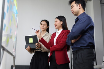 Asian businesswoman leading meeting with sticky notes on whiteboard and digital tablet.