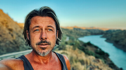 Middle aged tanned man with half long blond hair and grey stubble beard in singlet shirt walking outdoors during golden hour. Hills of Almogia, Malaga, Andalusia, Spain.