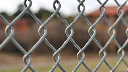 Fototapeta premium Close up of a weathered chain link fence with blurred outdoor background suggesting confinement or division