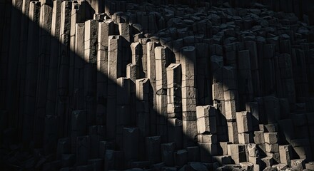 A dramatic beam of sunlight illuminates the geometric texture of dark basalt columns in a natural volcanic rock formation, creating a powerful abstract background with high contrast