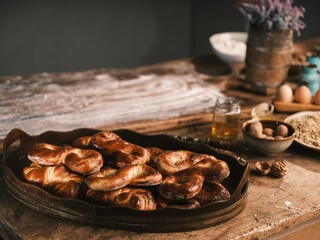 A wooden table displays a warm tray of Romanian mucenici, freshly baked and golden brown. Nearby, eggs and nuts complement the inviting atmosphere of homemade delights