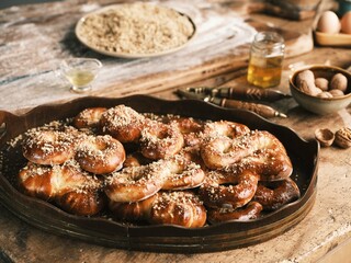 Freshly baked Romanian mucenici sit on a wooden platter, sprinkled with nuts. In the background, ingredients like flour and eggs hint at the traditional baking process
