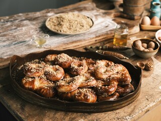 Freshly baked Romanian mucenici are beautifully arranged on a wooden platter, showcasing their golden color and nut topping. Nearby, flour and eggs create a cozy kitchen scene