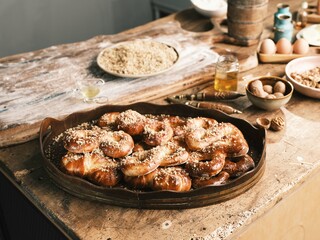 Freshly baked Romanian Mucenici decorate a rustic wooden tray, adorned with nuts. The warm kitchen exudes a welcoming atmosphere, perfect for celebrating tradition and flavor