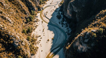 Stunning aerial top-down view of a winding river flowing through a deep rocky canyon with golden autumn foliage on the sunlit slopes