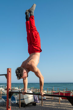 Man doing handstand on parallel bars at beach