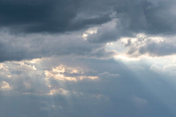 Dramatic sky with dark storm clouds and soft sun rays breaking through, creating a serene and atmospheric natural landscape
