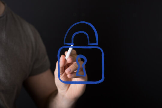 Man's hand drawing a blue virtual padlock icon on a dark background, representing cybersecurity, data protection, privacy, and secure digital ac