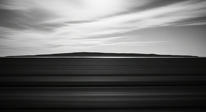 Serene and abstract monochrome landscape featuring a silhouetted island on the horizon with motion-blurred water in the foreground and a moody, cloudy sky