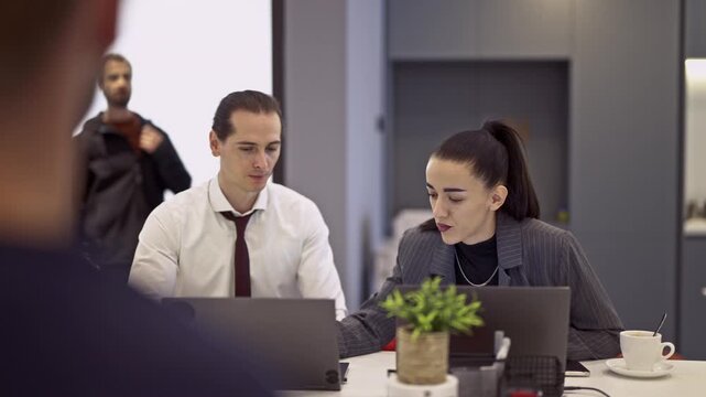 Professional business colleagues collaborate efficiently in a modern office environment. They are focused on their laptops during a productive meeting, discussing ideas and strategizing for success.