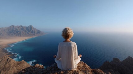 Woman sitting on a cliff overlooking the ocean. she is wearing a white dress and has blonde hair. the woman is meditating with her eyes closed and her hands resting on her knees.