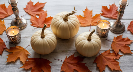 Three white pumpkins sit among orange autumn leaves and lit candles, creating a festive fall scene and showcasing the harvest season's beauty