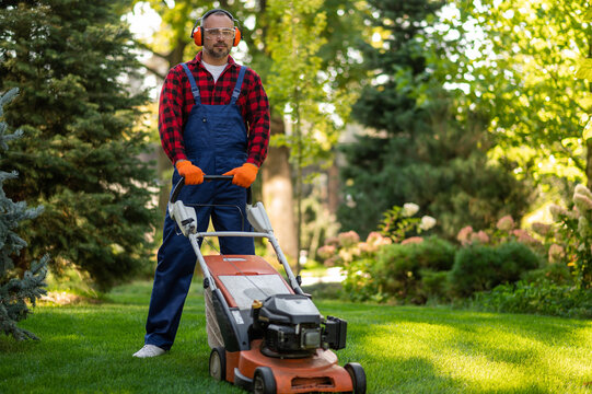 Male gardener standing with lawnmower on green grass - Powered by Adobe