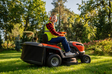 Fototapeta premium Worker in safety gear standing near lawn tractor in garden area
