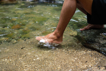 A bare foot gently touches the surface of clear, cool water in a natural stream.