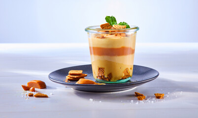 Karamell Dessert geschichtet in Einmachglas auf dunklem Dessertteller auf hellem Holzfond