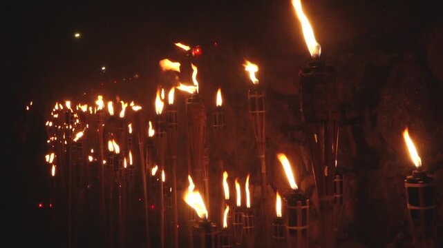 Close-up of a single lit bamboo torch with many others glowing in the blurred background, creating a warm and intense flame-filled atmosphere.