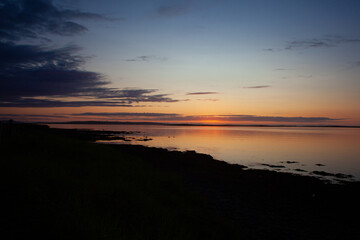 Obraz premium Sunset of gold and orange hovers on the horizon in midsummer over the sea on the island of Stronsay, Orkney, Scotland, UK
