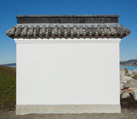 A blank wall painted white, with a layer of curved roof tiles, part of a pagoda or a blank wall.