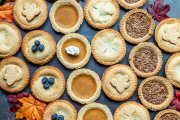 Delicious variety of fall pies arranged on a dark surface with colorful autumn leaves
