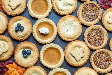 Variety of delicious mini pies arranged on a table with autumn leaves during a cozy fall gathering
