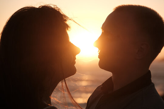 Silhouetted couple facing each other with the setting sun between them, creating a romantic and intimate golden hour moment.