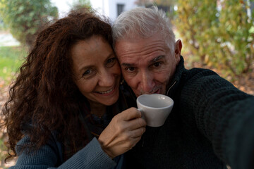 Happy senior couple taking a selfie while drinking coffee together outdoors