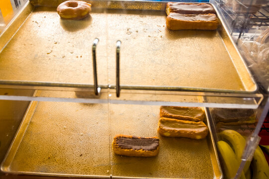 Donuts and cakes with chocolate icing on a tray in a shop window, a few left.
