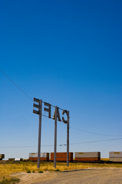 Cafe Sign, large letters on tall posts on flat land, above a railroad with containers. 