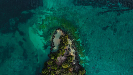 Obraz premium Overhead view of a small, secluded tropical island or islet surrounded by deep turquoise and emerald clear water