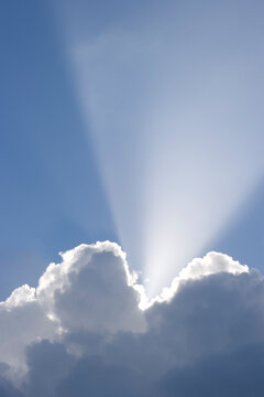 Sun shining behind cumulonimbus clouds in a blue sky. 