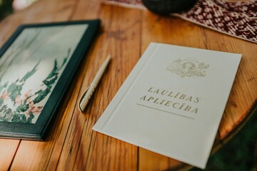Valmiera, Latvia - June 15, 2019: Elegant wedding invitation booklet on wooden table with framed photo and decorative elements in soft natural light