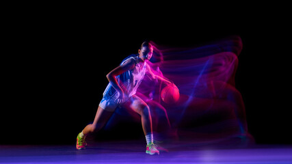 Female basketball player dribbling with ball in glowing studio motion. Concept of fitness...