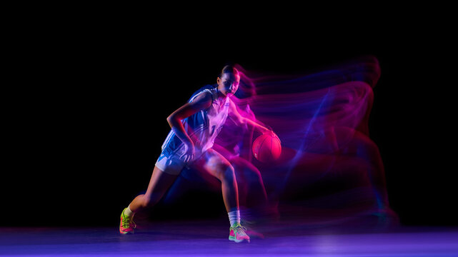 Female basketball player dribbling with ball in glowing studio motion. Concept of fitness promotion, motivation visuals, sports branding, and energetic lifestyle ads. - Powered by Adobe
