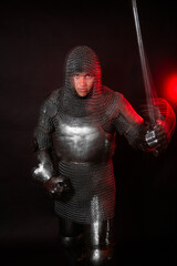 Fototapeta premium A medieval knight in full armor poses against a dark background with red backlighting. Long-exposure photo with motion blur.