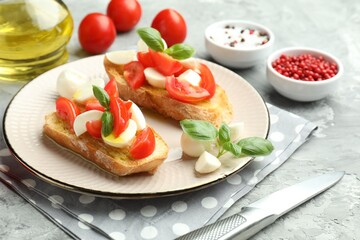 Tasty bruschettas with mozzarella cheese, tomatoes, basil and spices on grey textured table, closeup