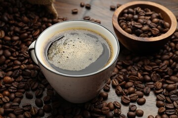 Aromatic coffee in cup and beans on wooden table, closeup
