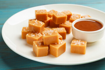 Tasty candies with salt and caramel sauce on light blue wooden table, closeup