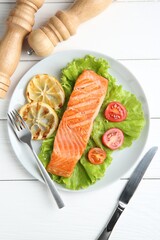 Piece of tasty grilled salmon, lemon slices and salad on white wooden table, flat lay