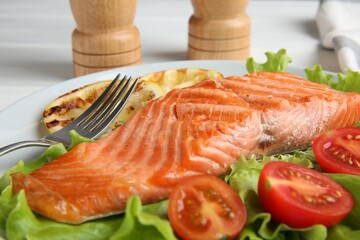 Piece of tasty grilled salmon, lemon slices and salad on white table, closeup