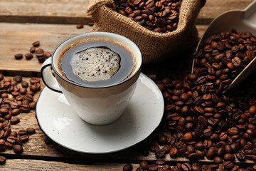 Aromatic coffee in cup and beans on wooden table, closeup