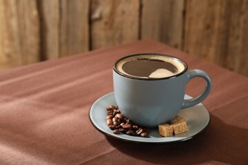 Aromatic coffee in cup, beans and brown sugar on table, closeup. Space for text