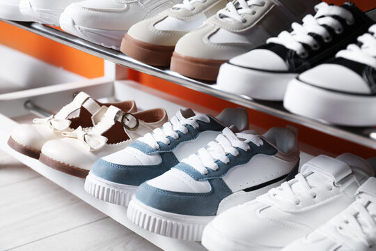 Different kid's shoes on shelves near orange wall indoors, closeup - Powered by Adobe