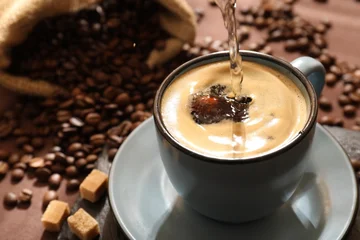 Selbstklebende Fototapeten Cafe Pouring aromatic coffee into cup, beans and brown sugar at table, closeup  © New Africa