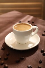 Aromatic coffee in cup and beans on table, closeup