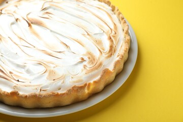 Tasty lemon meringue tart on yellow background, closeup