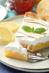 Slice of tasty lemon meringue tart with mint served on blue table, closeup